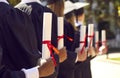 Diverse college or university graduates with diplomas at outdoor graduation ceremony