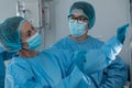 Diverse couple of male and female surgeons in operating theatre wearing face masks looking at screen