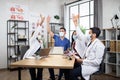 Diverse doctors in protective masks throwing up papers after meeting in modern office