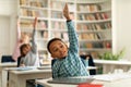 Diverse elementary school students raising hands to answer teacher questions, sitting at desks in classroom interior Royalty Free Stock Photo