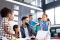 Diverse elementary schoolchildren and male teacher using laptop, talking in classroom