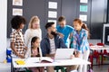 Diverse elementary schoolchildren and male teacher using laptop, talking in classroom