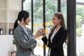 Diverse employees chatting during coffee break, walking in modern office, Asian businesswoman wearing glasses sharing Royalty Free Stock Photo