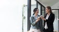 Diverse employees chatting during coffee break, walking in modern office, Asian businesswoman wearing glasses sharing Royalty Free Stock Photo