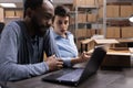 Diverse employees sitting at table in warehouse checking transportation logistics on laptop computer Royalty Free Stock Photo