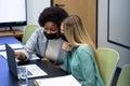 Diverse female business colleagues wearing masks talking and using laptop in meeting room Royalty Free Stock Photo