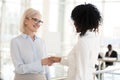 Smiling diverse female colleagues handshake meeting in hallway