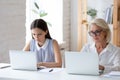 Diverse female employees work on laptops in office