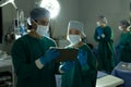 Diverse female and male surgeon in discussion, using tablet in operating theatre during operation