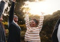 Group of multiethnic friends standing together raising their arms and enjoying in the park on summer day