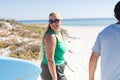 Diverse friends, including a young Caucasian woman and a biracial man, enjoy a sunny beach day Royalty Free Stock Photo