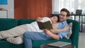 Diverse gay couple lying on couch and reading book together. Royalty Free Stock Photo
