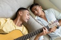 Diverse gay male couple lying on sofa playing guitar Royalty Free Stock Photo