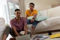 Diverse gay male couple sitting in living room using laptop and learning Royalty Free Stock Photo