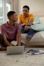 Diverse gay male couple sitting in living room using laptop and learning Royalty Free Stock Photo