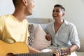Diverse gay male couple sitting on sofa playing guitar and smiling Royalty Free Stock Photo