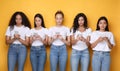 Diverse Girls Using Smartphones Texting Standing Over Yellow Background Royalty Free Stock Photo