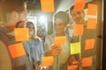 Diverse group of businesspeople standing in an office brainstorming together with sticky notes on a glass wall Royalty Free Stock Photo