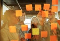 Diverse group of businesspeople standing in an office brainstorming together with sticky notes on a glass wall Royalty Free Stock Photo