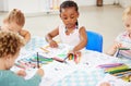 Diverse group of children sitting at a table and colouring at pre-school or kindergarten. Group of kids with colourful Royalty Free Stock Photo