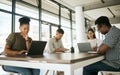 Diverse group of entrepreneurs business people working on laptops and writing notes while sitting around a table in a Royalty Free Stock Photo