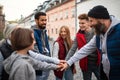 Diverse group of happy community service volunteers stacking hands together outdoors in street