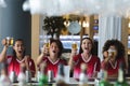 Diverse group of male and female sports fans raising glasses and watching game at bar