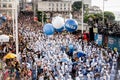 Diverse group of people joyfully marching in a parade, with blue clothes and balloons