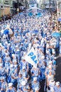 Diverse group of people joyfully marching in a parade, with blue clothes and umbrellas