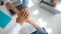 Close-up of diverse business team stacking hands in with laptops and documents on white desk symbolizing teamwork and Royalty Free Stock Photo