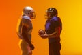 Diverse male american football players holding ball with neon orange lighting