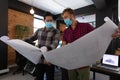 Diverse male colleagues wearing masks in disucssion holding architectural plans in office Royalty Free Stock Photo