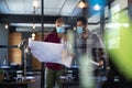 Diverse male colleagues wearing masks in disucssion holding architectural plans in office Royalty Free Stock Photo