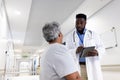 Diverse male doctor with tablet talking to senior patient on hospital bed Royalty Free Stock Photo