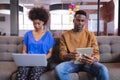 Diverse male and female colleagues working sititng on sofa in office using computer and tablet Royalty Free Stock Photo