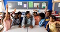 Diverse male teacher using tablet with children raising hands in class at elementary school Royalty Free Stock Photo