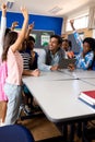 Diverse male teacher using tablet with children raising hands in class at elementary school Royalty Free Stock Photo