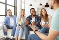 Diverse millennial friends talking and laughing together, drinking tea or coffee at home