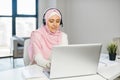 A young muslim woman wearing hijab using a laptop and a headset Royalty Free Stock Photo