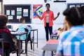 Diverse pupils sitting at desks listening to female teacher at front of class