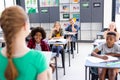 Diverse pupils sitting at desks listening to schoolgirl reading to class, copy space