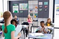 Diverse pupils sitting at desks listening to schoolgirl reading to class