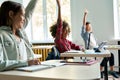 Diverse schoolkids sitting at desk raising hands answering at lesson. Royalty Free Stock Photo