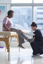 Diverse senior female patient exercising leg and female doctor advising in hospital room