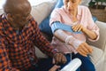 Diverse senior man testing blood pressure of senior woman in sunny living room Royalty Free Stock Photo