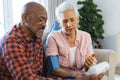 Diverse senior man testing blood pressure of senior woman in sunny living room Royalty Free Stock Photo