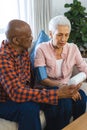 Diverse senior man testing blood pressure of senior woman in sunny living room Royalty Free Stock Photo