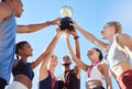 A diverse team of athletes celebrating a victory with a golden trophy and looking excited. A fit and happy team of