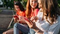 Diverse three girl friends using their phones outdoors. Group gen z young people using mobile smartphone sitting on Royalty Free Stock Photo