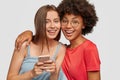 Diverse women with cheerful expressions read posts in social networks via cellular, hug and smile positively, model Royalty Free Stock Photo